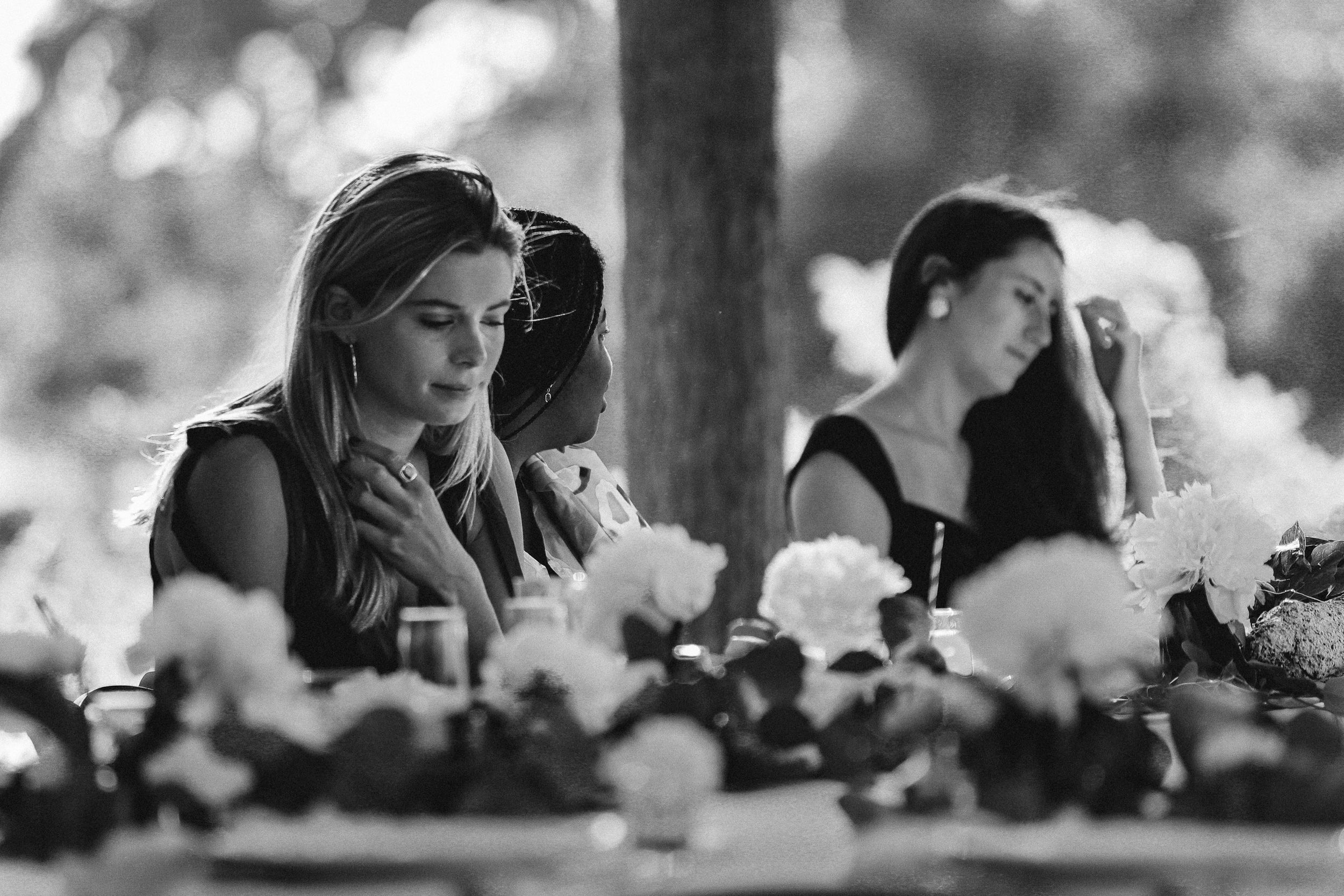 A candid black and white photo showing emotion at an elegant outdoor table setting with flowers.