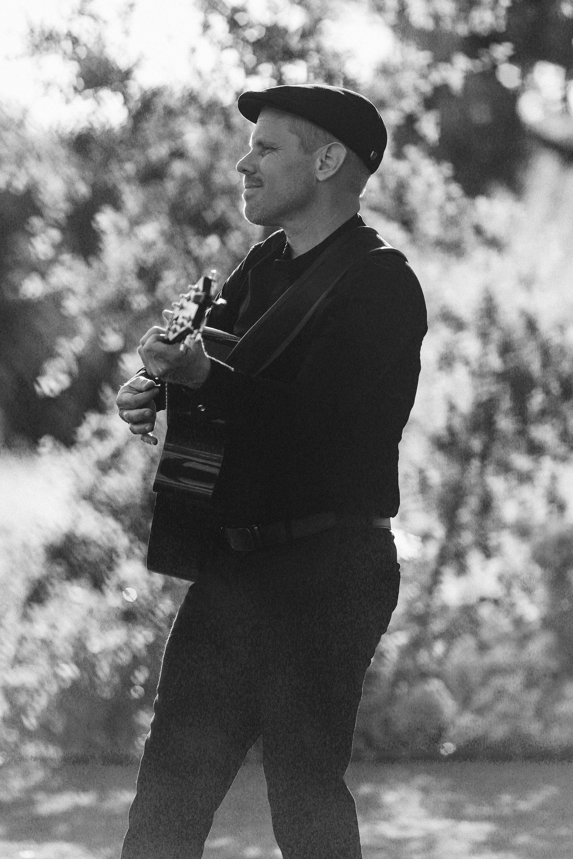 A black and white portrait of a musician playing acoustic guitar outdoors.