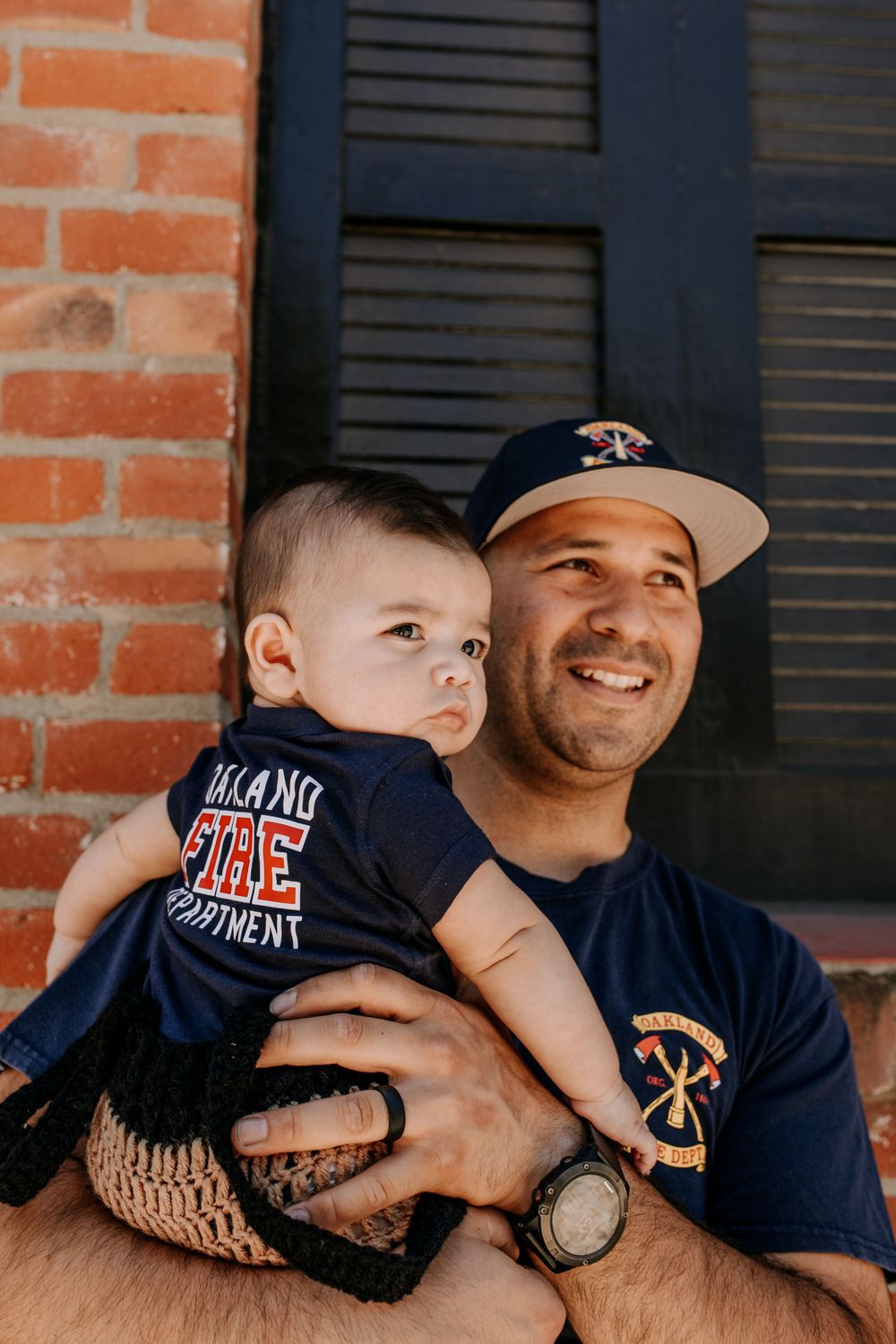 Adult and baby in matching navy outfits posing against brick wall.
