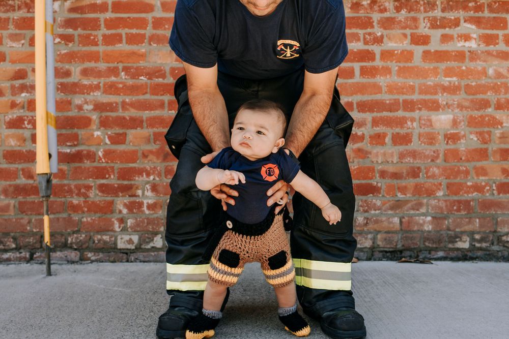 Firefighter in protective gear sitting with baby in matching uniform outfit.