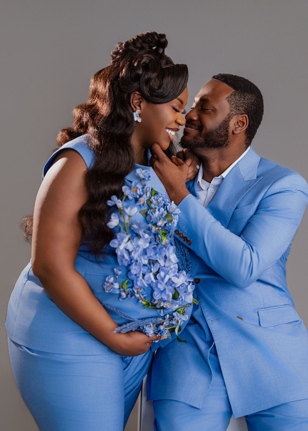 A romantic couple in matching light blue outfits embrace while holding blue delphinium flowers during a photo session.