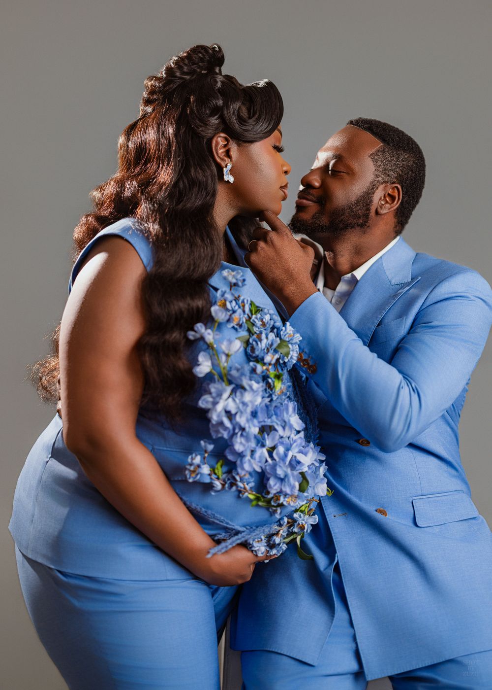 A romantic couple in blue attire share an intimate moment while holding a bouquet of blue hydrangeas.
