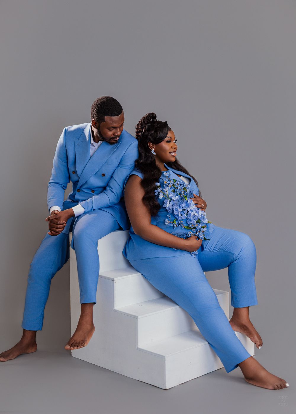 A couple in coordinating blue outfits poses barefoot on white steps during a stylish photoshoot.