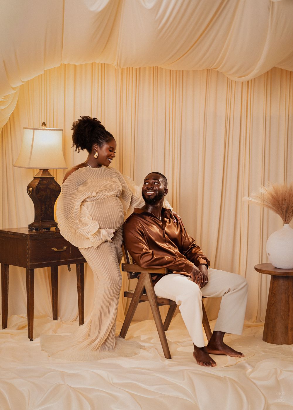 A couple in warm tones share a joyful moment in an elegant cream-colored room with draped fabric walls and furniture.