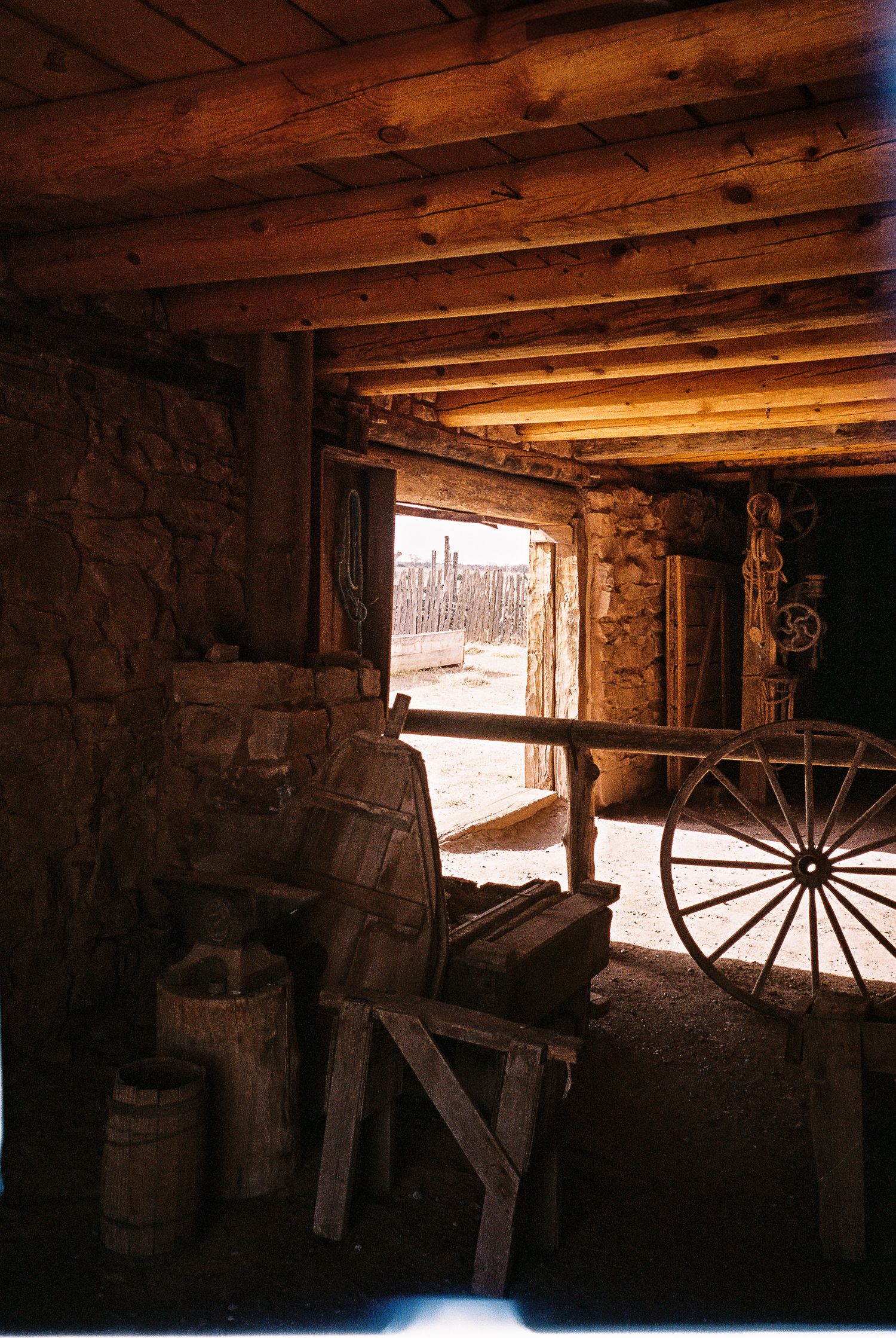 Interior view of a rustic barn or workshop with wooden beams and wagon wheels visible in silhouette.