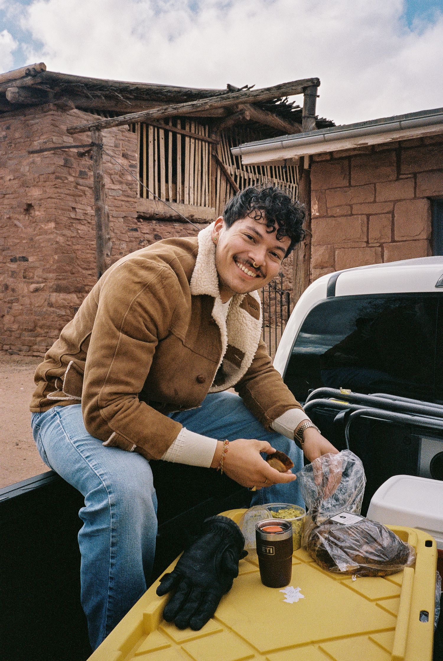 Person in brown jacket working on yellow surface of truck bed in front of brick wall.