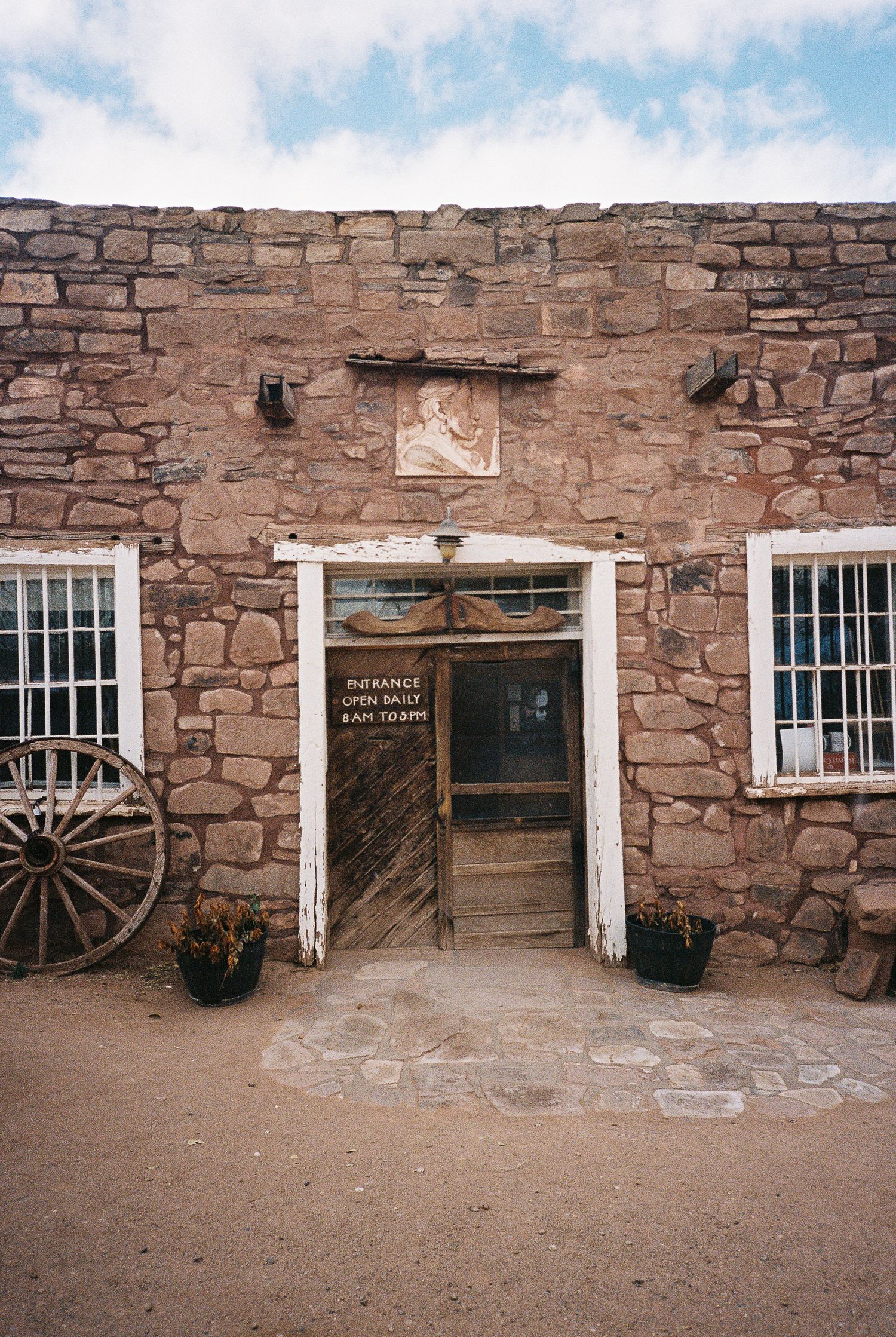 Historic stone building facade with white-framed windows and wooden wagon wheels displayed outside.