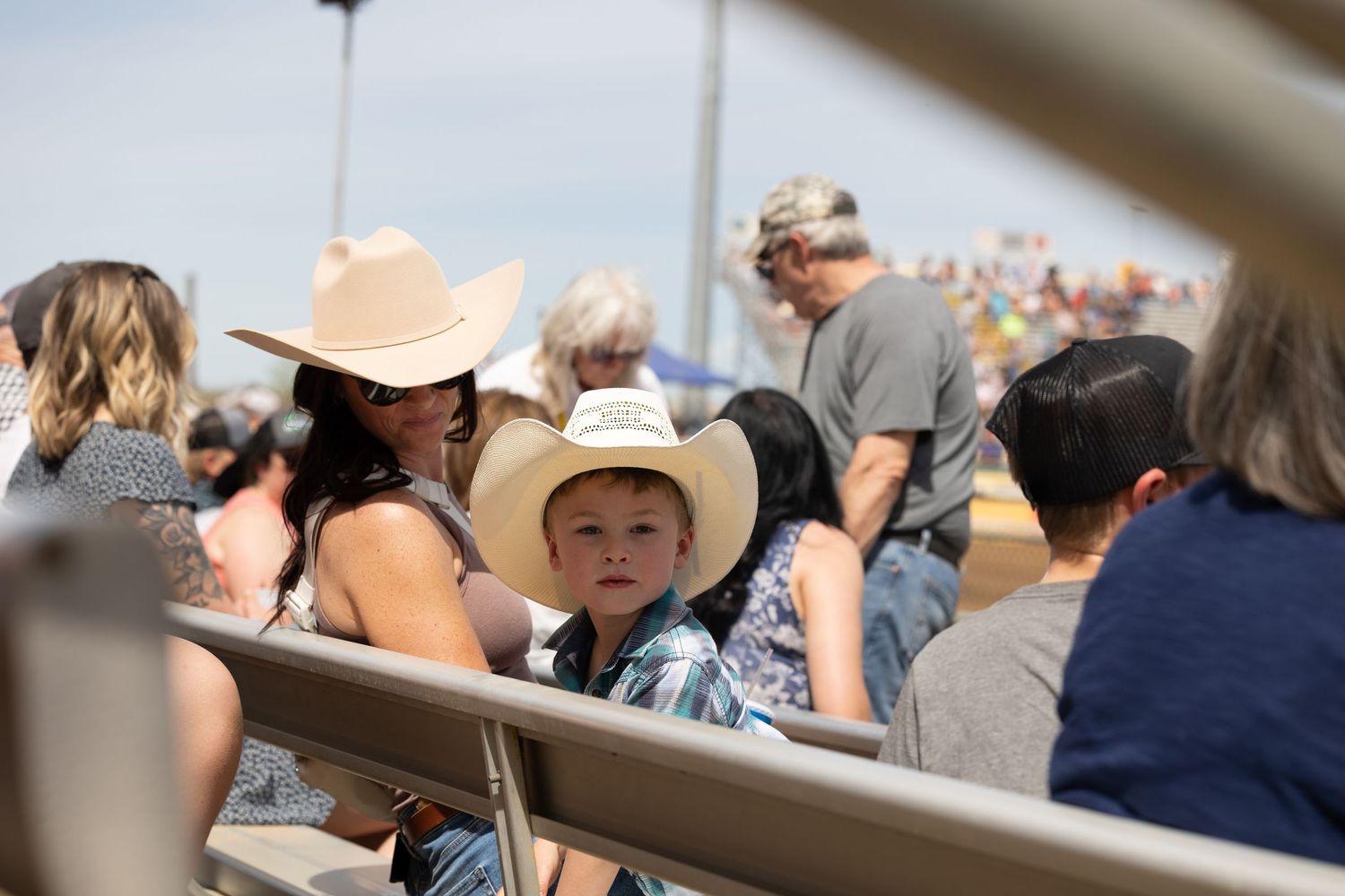 Spectators in cowboy hats watch from bleacher seating at a Western rodeo event.