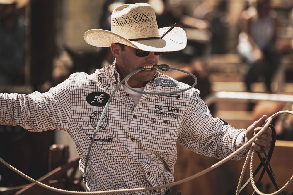 Cowboy in checkered shirt working with rope at rodeo competition.