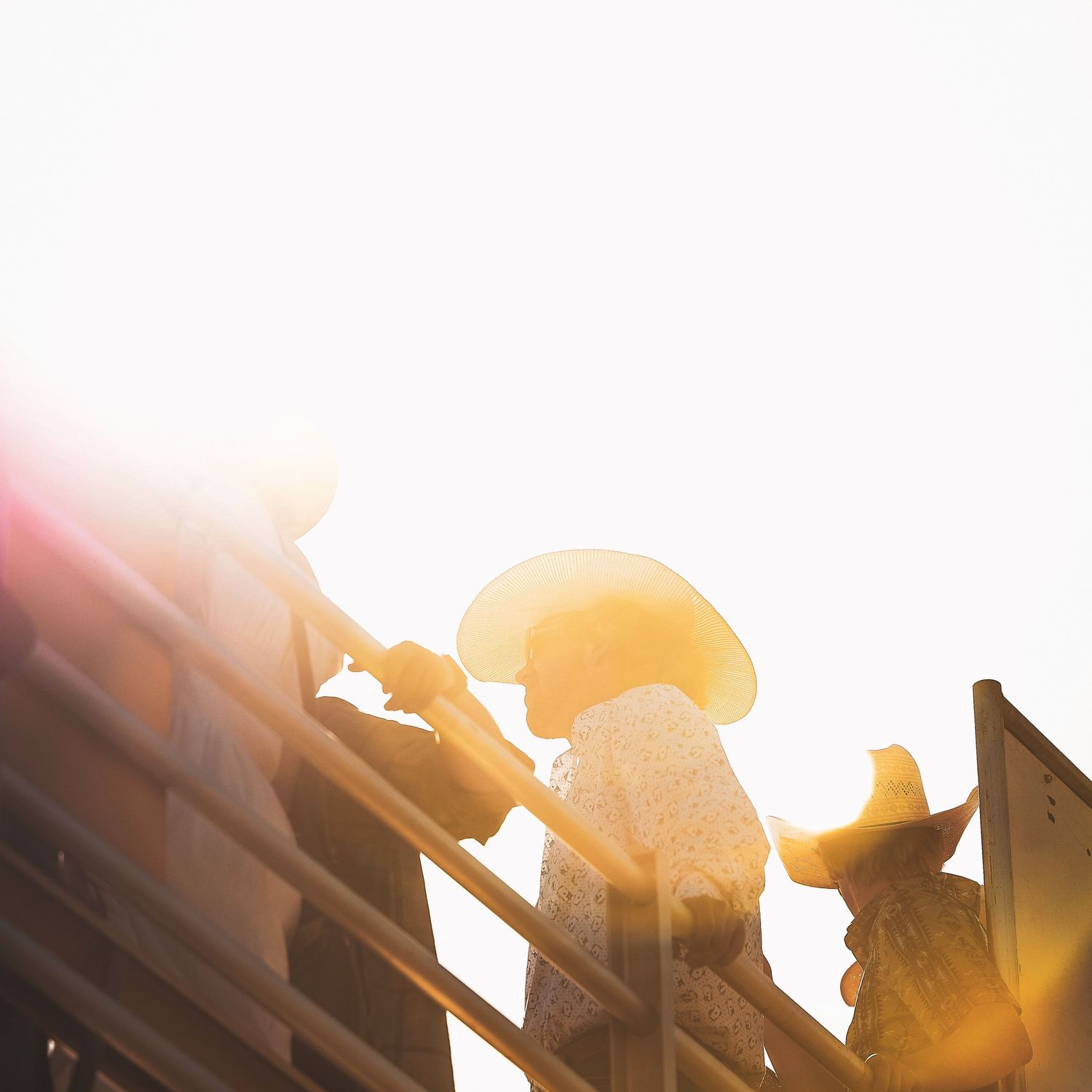 Silhouetted cowboy hats against a bright sunset at a rodeo event.