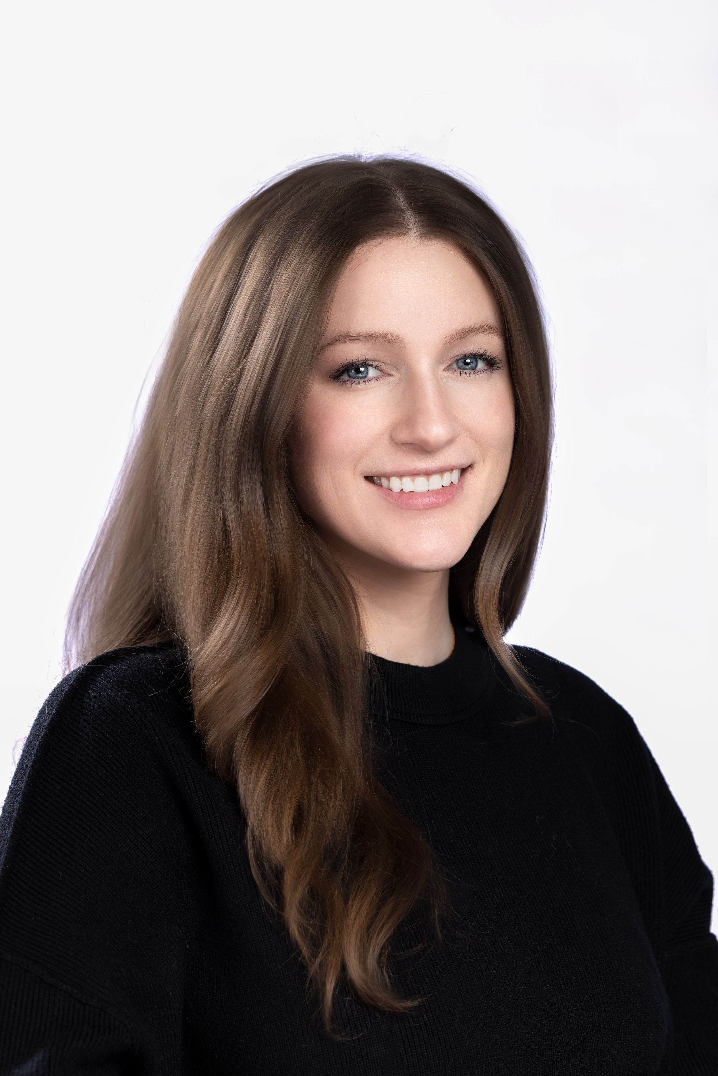 Professional headshot of someone smiling wearing a black sweater against a white studio background.