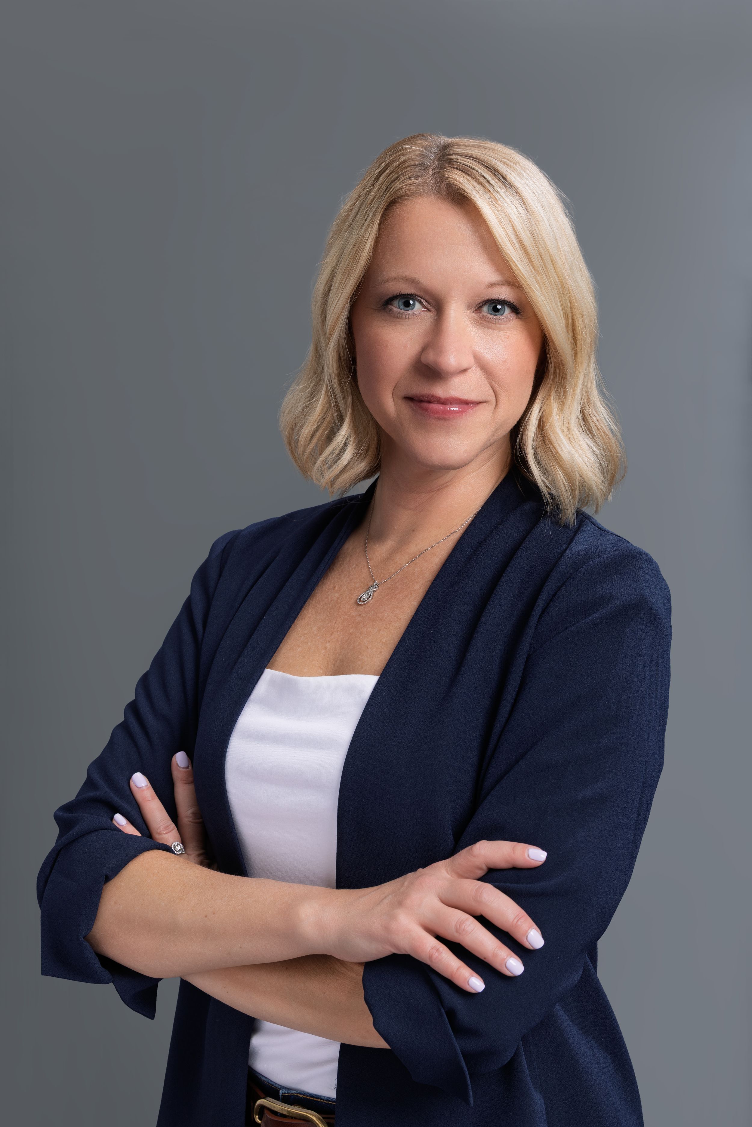 Professional headshot series showing various poses in a navy blazer and white top against a gray backdrop.