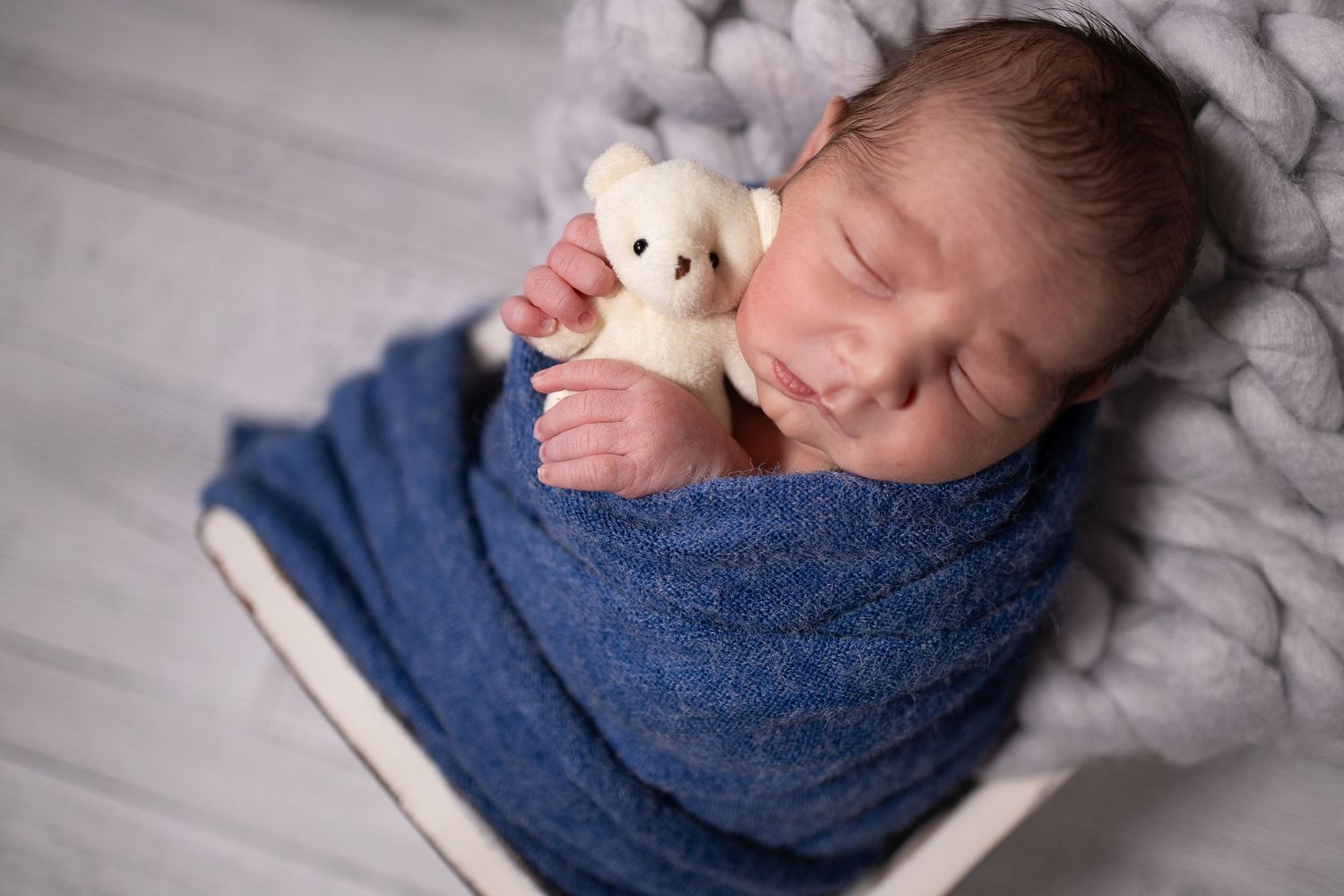 Sleeping newborn baby photographed on beige fur with natural elements.