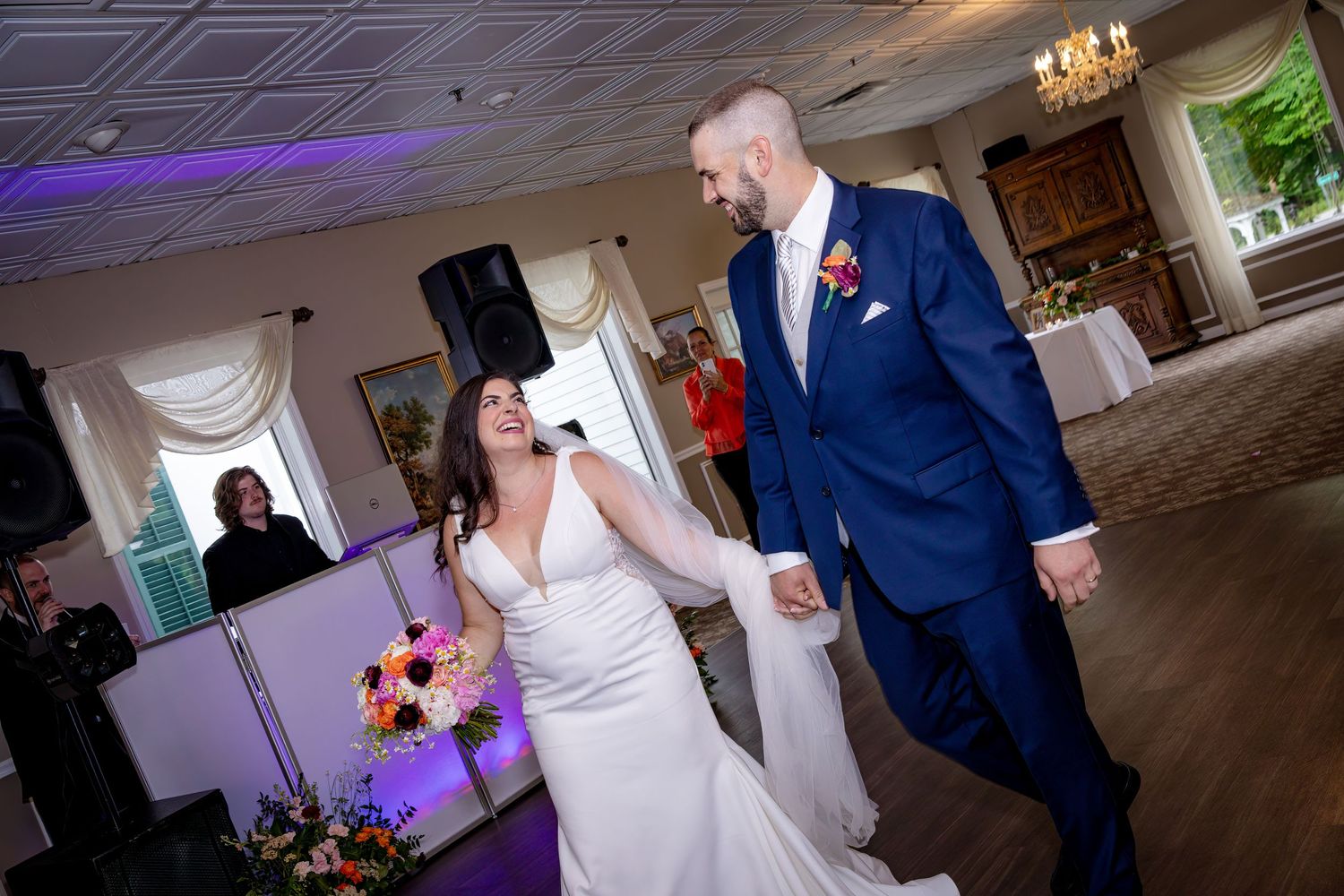 A joyful couple shares their first dance at their wedding reception in an elegant banquet hall with purple lighting.