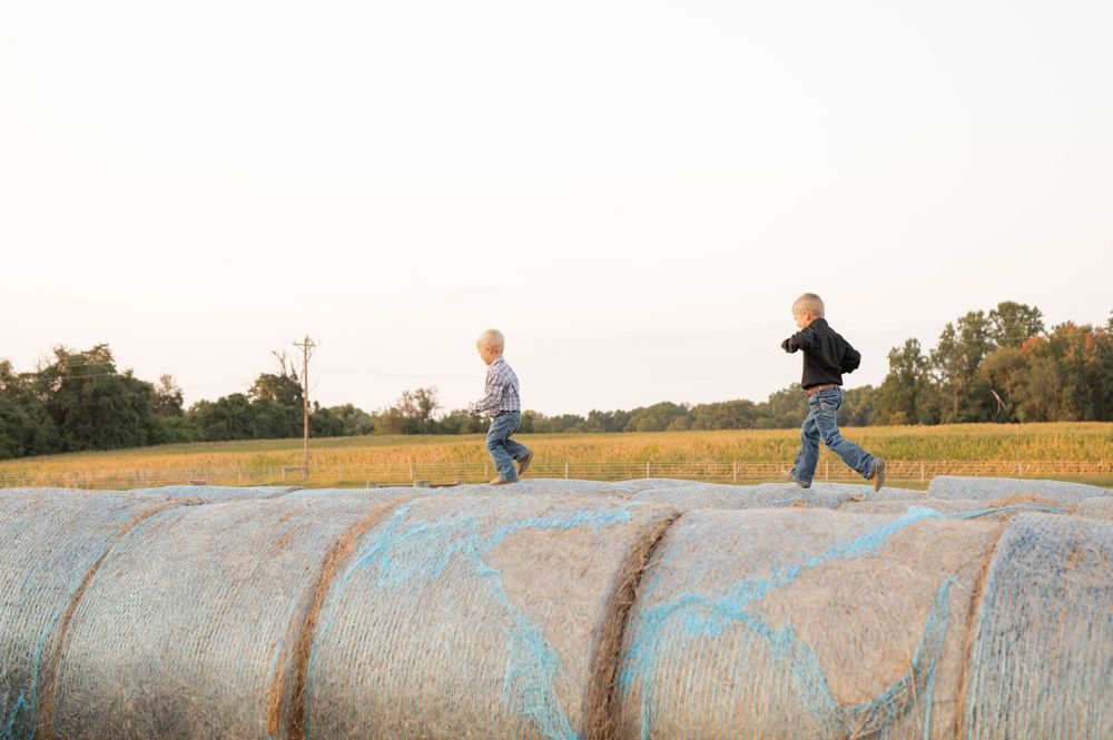 Children playing and running on hay bales in rural field at sunset.