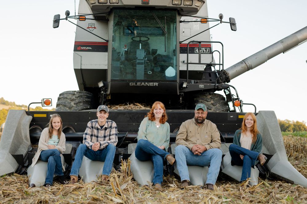 Group of farmers sitting on large combine harvester in agricultural field.