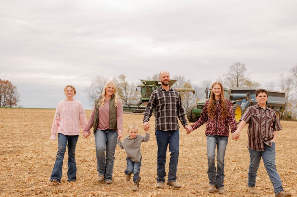 Family standing together in harvested agricultural field on cloudy day.