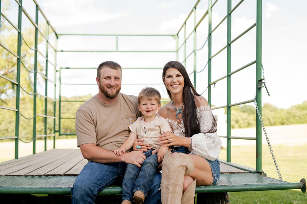 Family sits together on green wooden wagon platform for outdoor portrait.