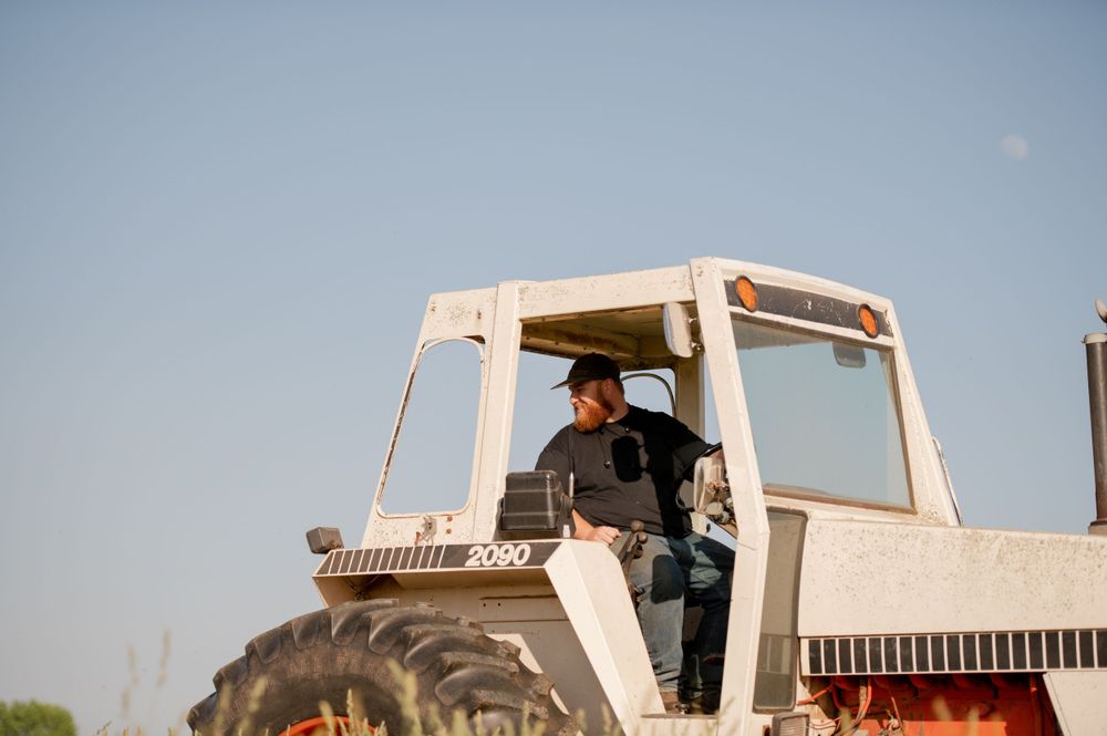 Farmer operating a large white tractor in a rural field against blue sky.