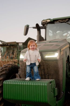 Small child stands excitedly on green tractor in evening light.