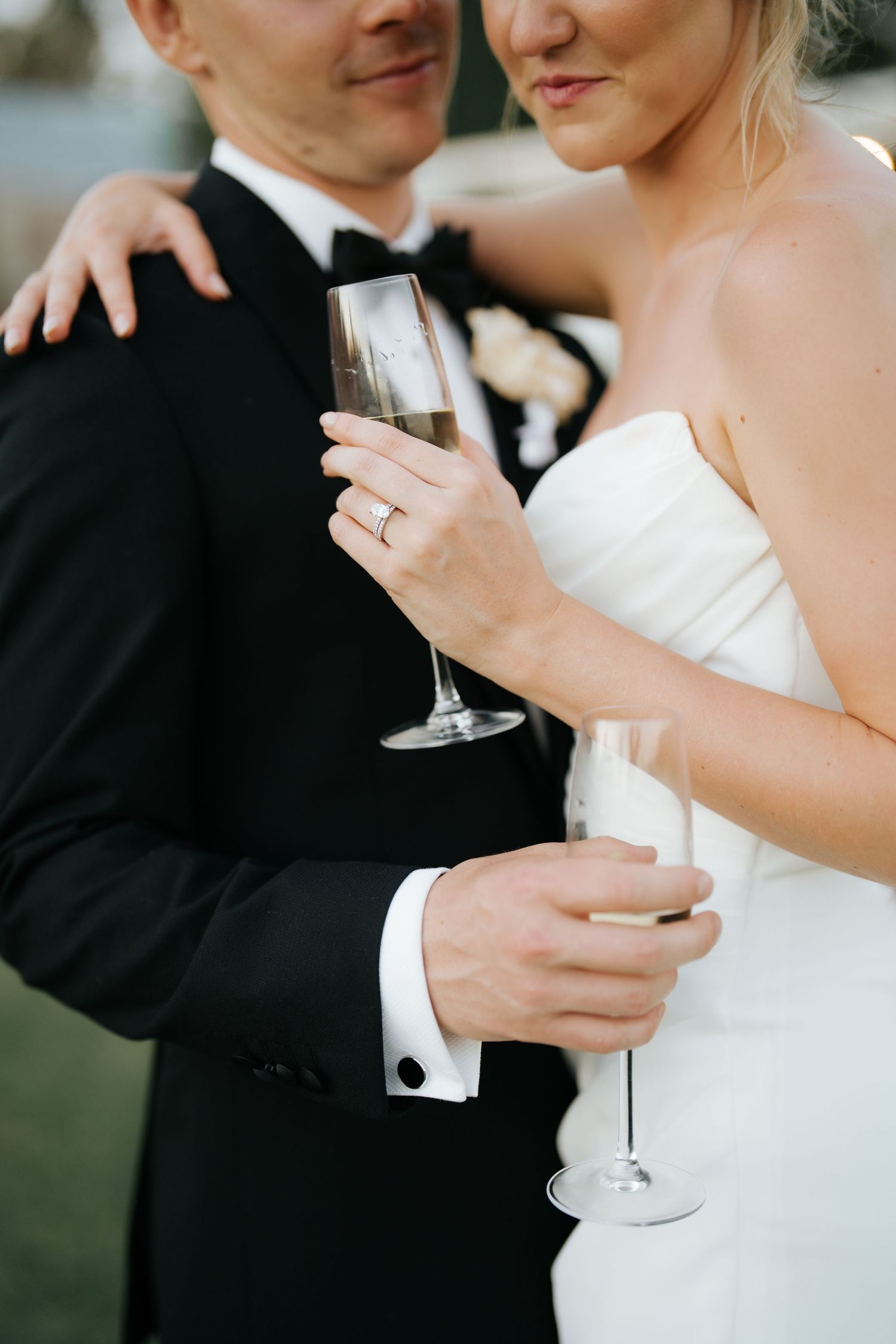 Bride and groom hold champagne flutes together, showcasing her diamond ring at their wedding reception.