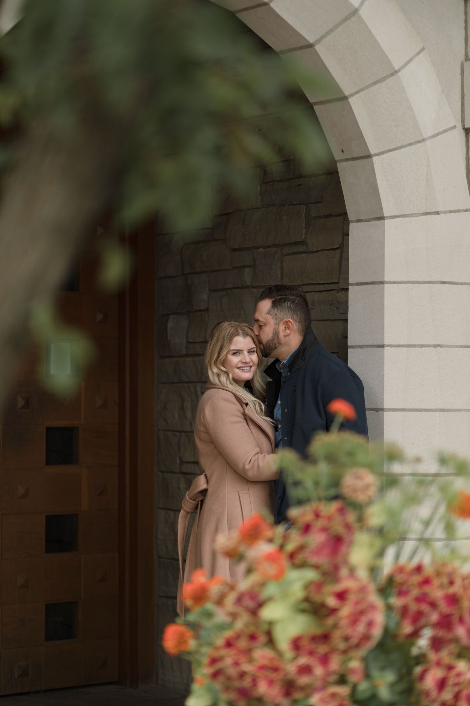 Romantic couple embracing in an archway with colorful flowers in the foreground on a fall day.