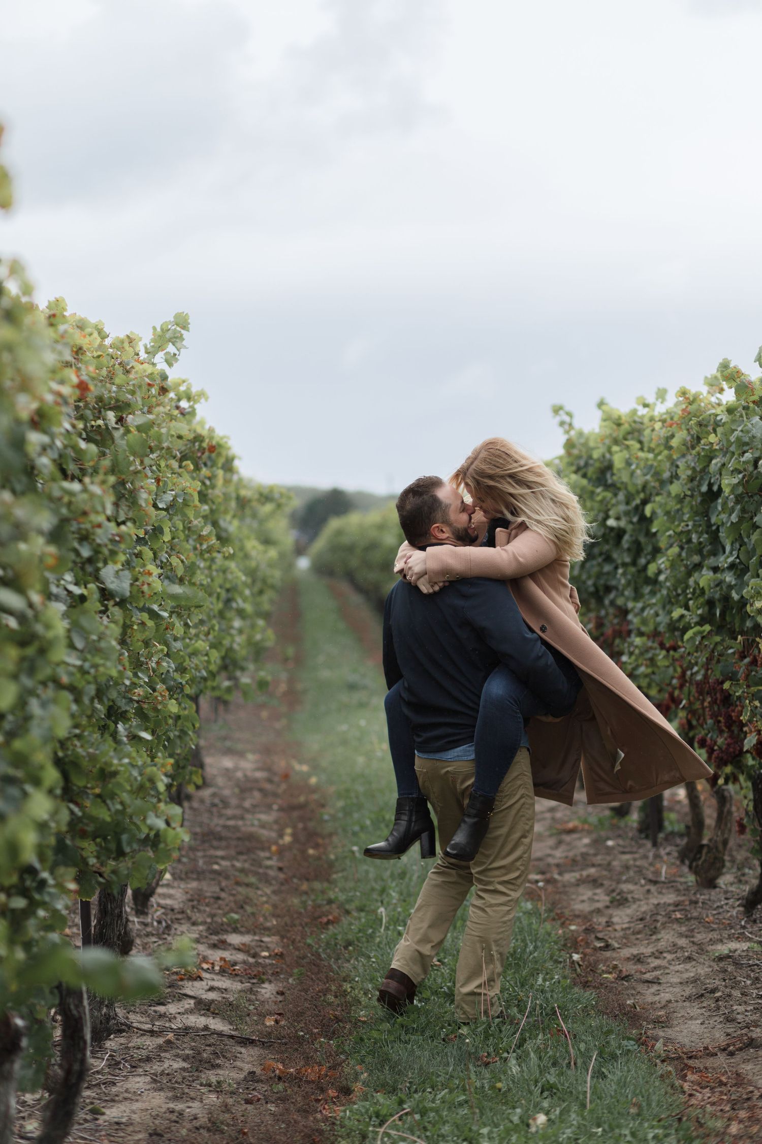 A romantic embrace between a couple in a scenic vineyard with rows of grapevines stretching into the distance.