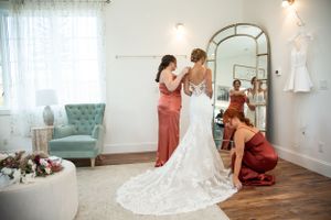 Wedding dress preparation scene in bridal suite with mint green chair and arched mirror.