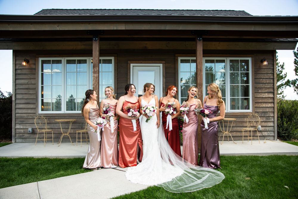 Bridesmaids in pink and mauve dresses gathered with bride outside rustic wedding venue.