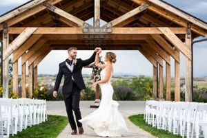 A celebratory moment under a rustic wooden pavilion with white chairs set up for an outdoor wedding ceremony.