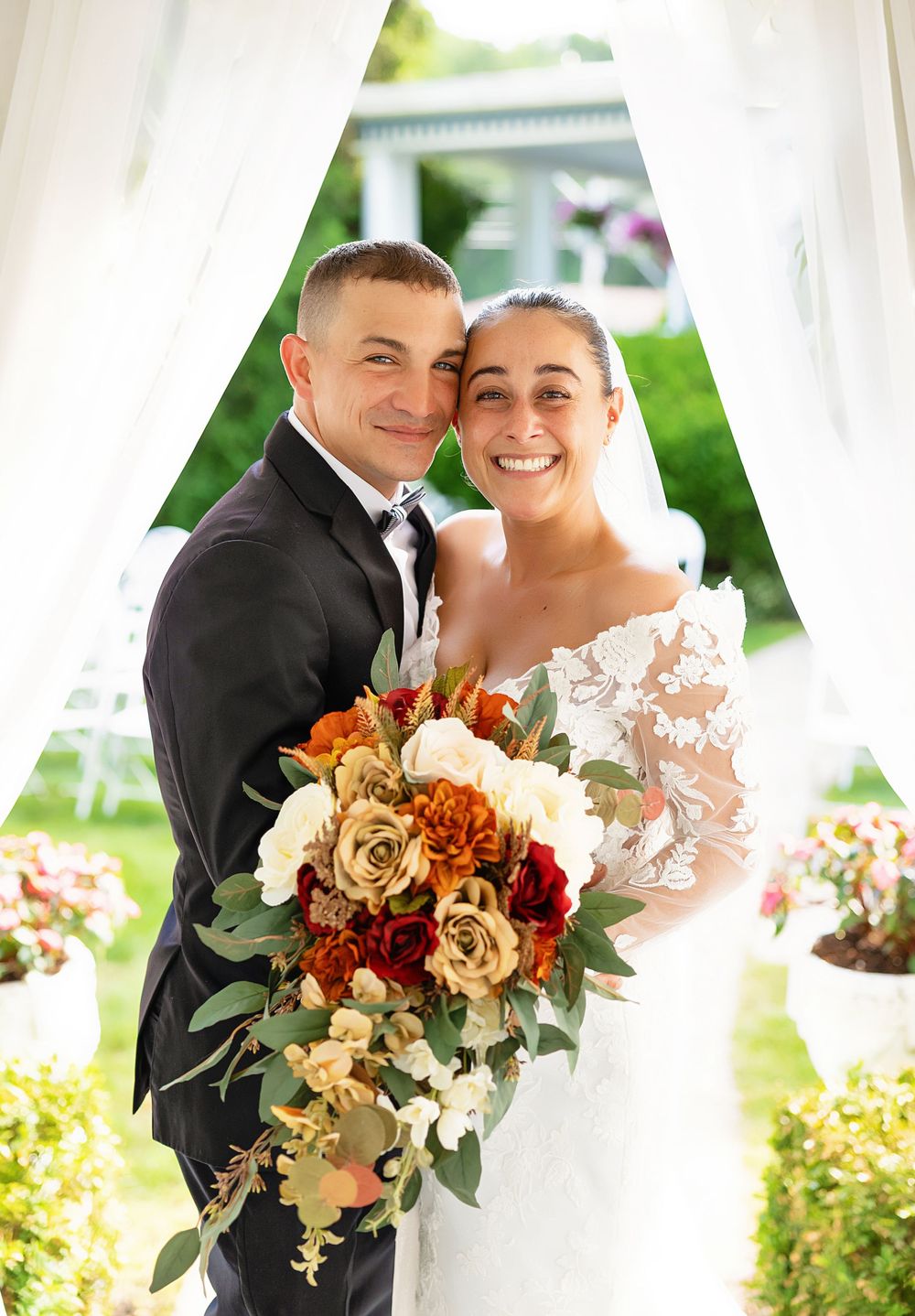 A romantic autumn wedding scene with a couple embracing under white drapes, surrounded by orange and cream floral bouquets.