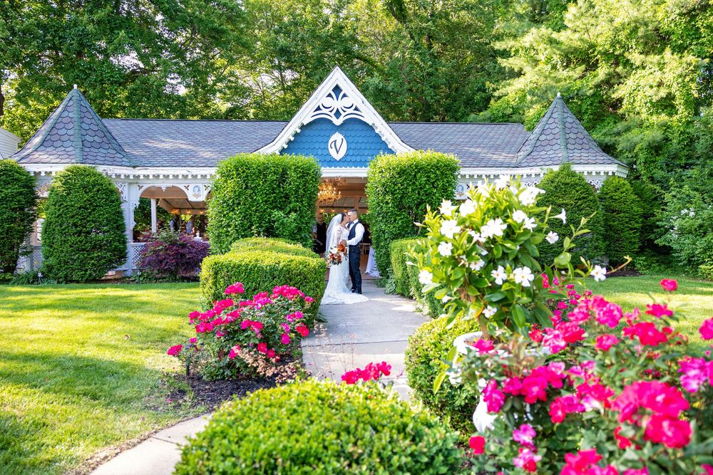 A lush garden path lined with vibrant pink roses and green shrubs leads to a white gazebo in summer.