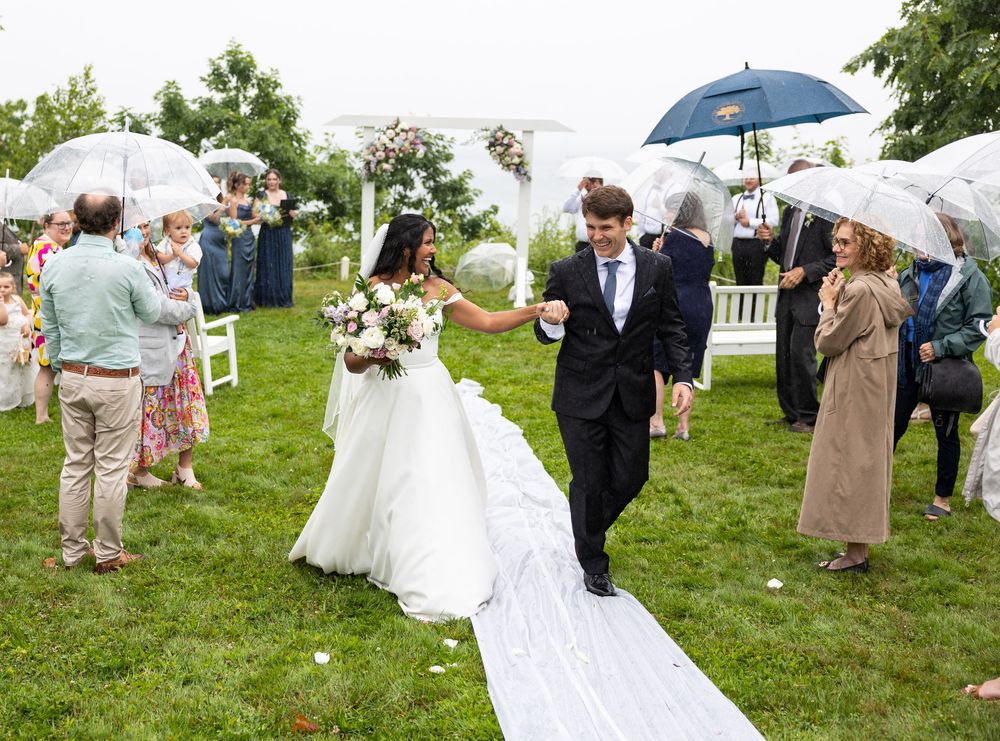 A wedding celebration on a rainy day with guests holding umbrellas on a green lawn during the ceremony.