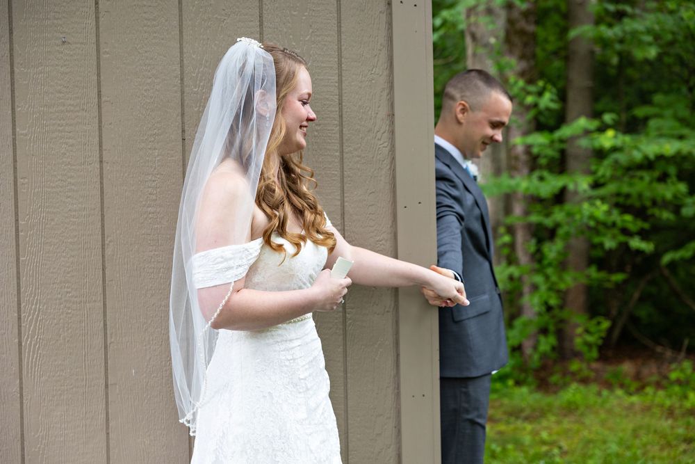 A bride in a white wedding dress and veil walks through a wooded outdoor setting during a wedding ceremony.