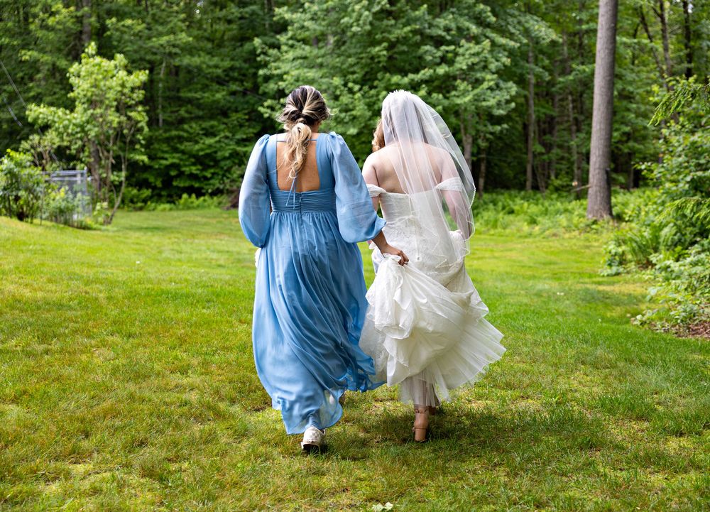 Two people in formal attire walk hand in hand through a lush green garden on a sunny summer day.