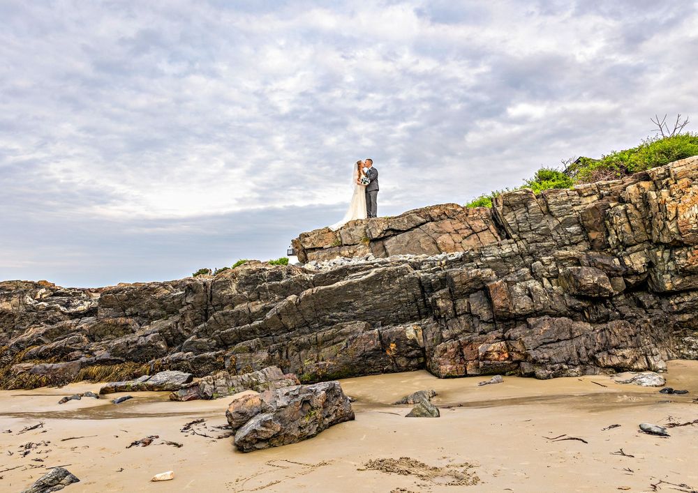 Panoramic view of a rocky coastal beach with cloudy skies and cliffs in the background.