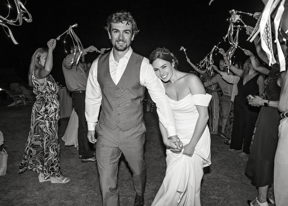 Wedding couple and guests dance joyfully together on a dark dance floor at an evening reception celebration.