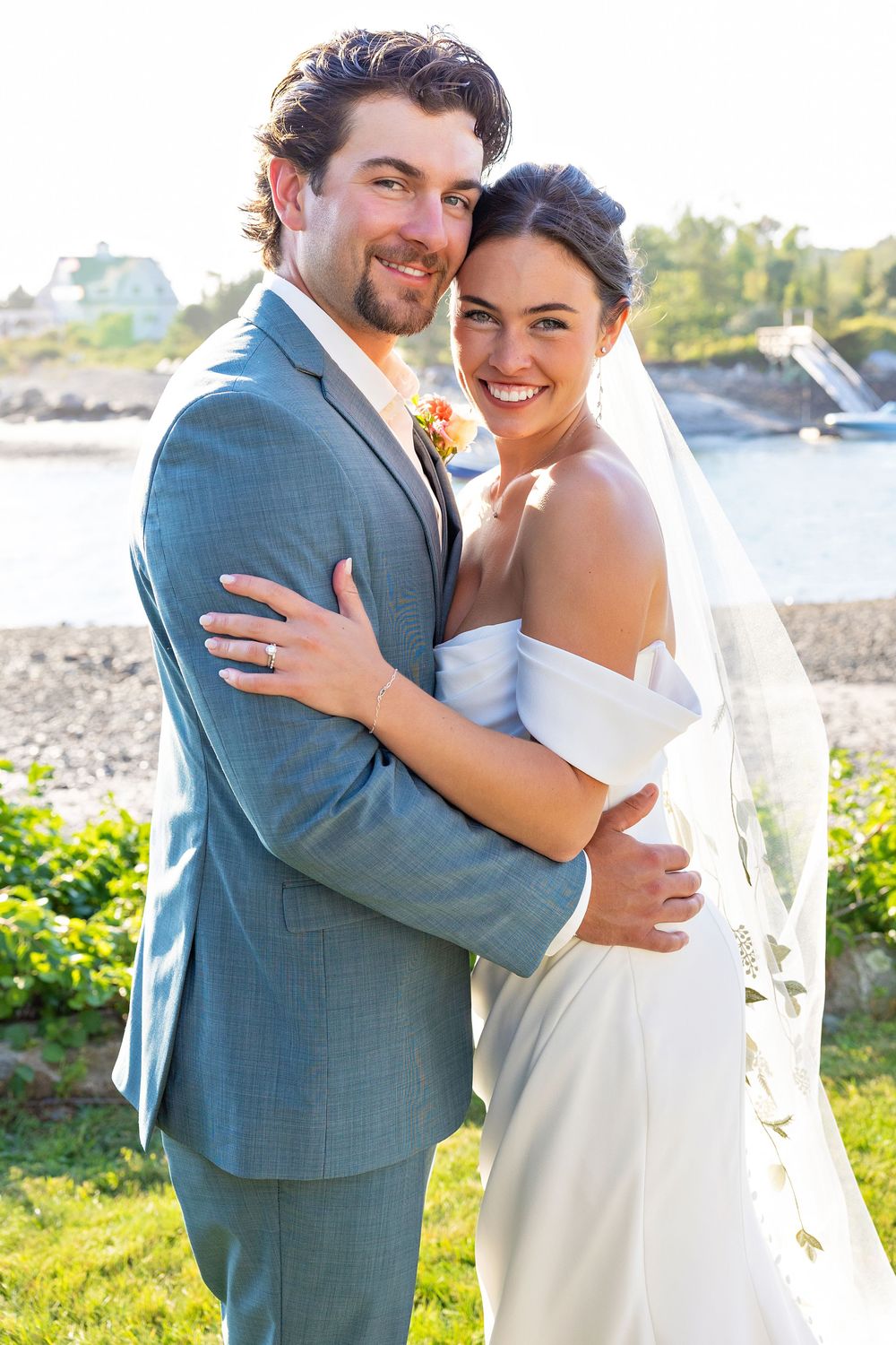 A romantic wedding photo series shows a couple embracing outdoors by the water on a sunny summer day.