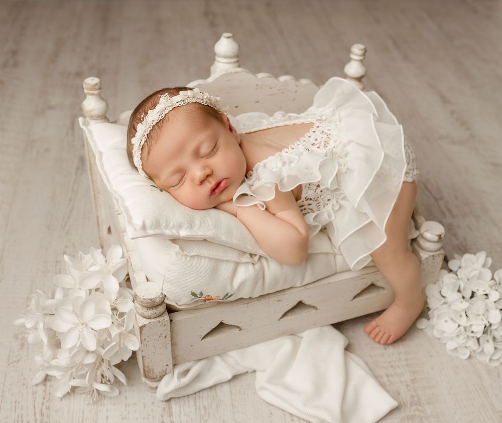 A sleeping baby rests peacefully on a decorative white wooden bed with lace details and floral accents.