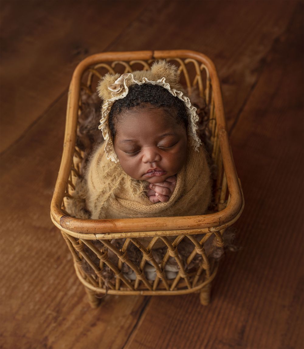 A sleeping newborn nestled in a cozy wicker basket with soft blankets and delicate decorative elements. Argyll and Bute newborn photographer