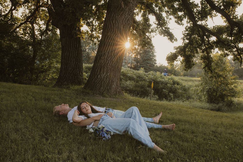 A couple relaxes together on a grassy hillside during golden hour as sunlight filters through oak trees.