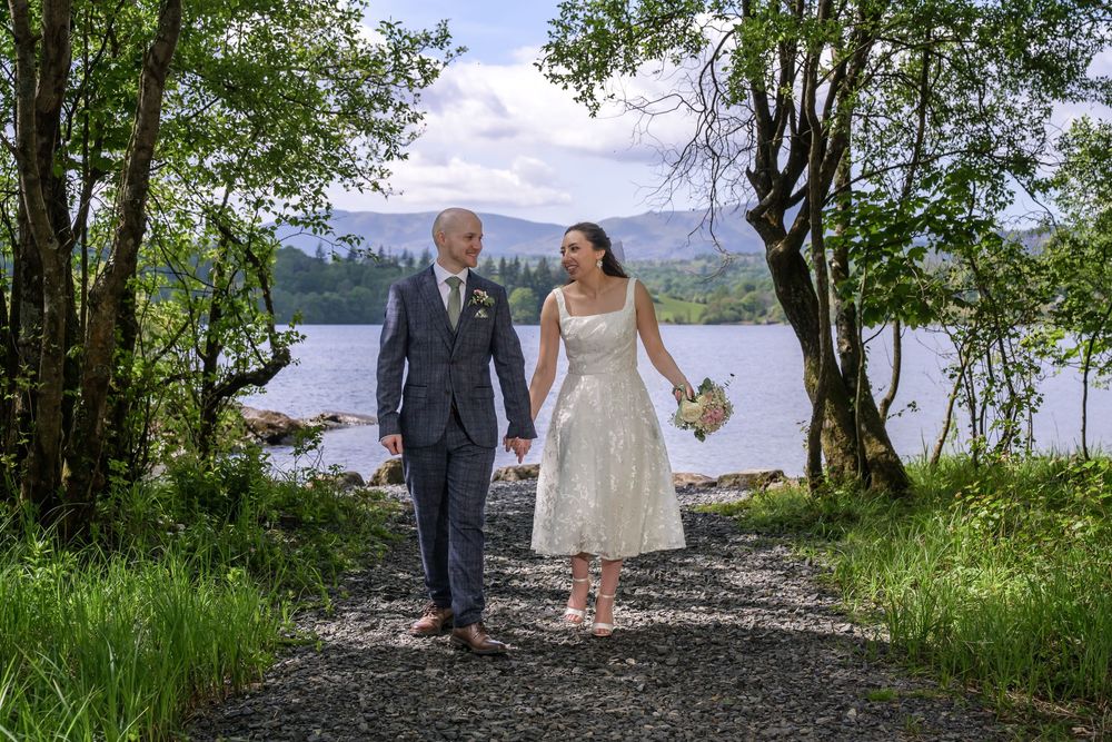 Bride and groom walking under trees with lake behind at Cragwood Country House wedding