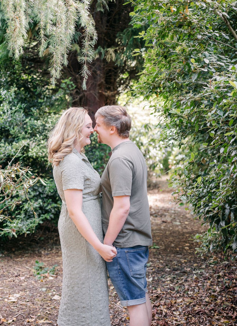 A romantic couple shares tender moments along a wooded garden path surrounded by lush greenery.