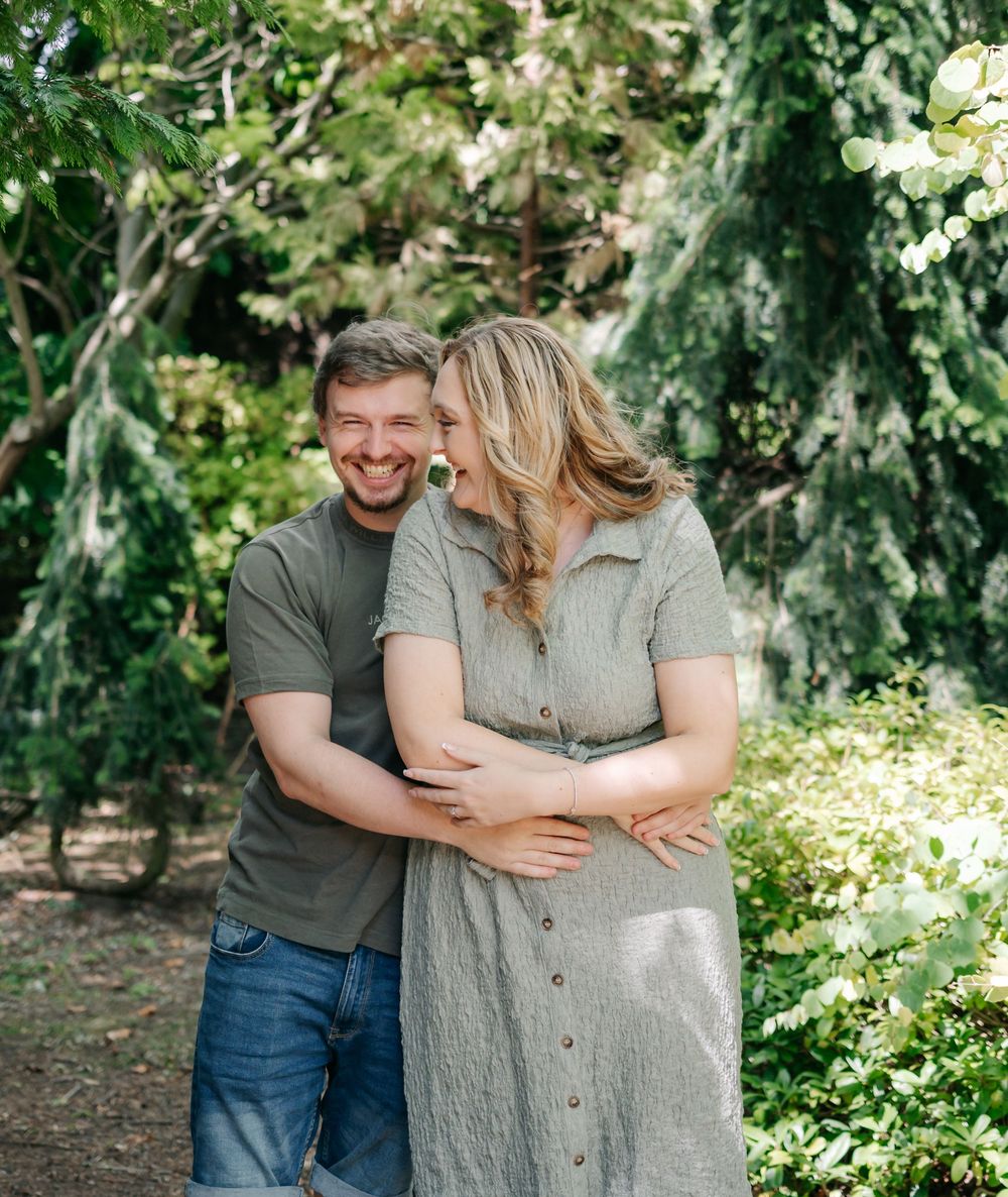 Couple embracing outdoors in a lush green garden setting in springtime with dappled sunlight.