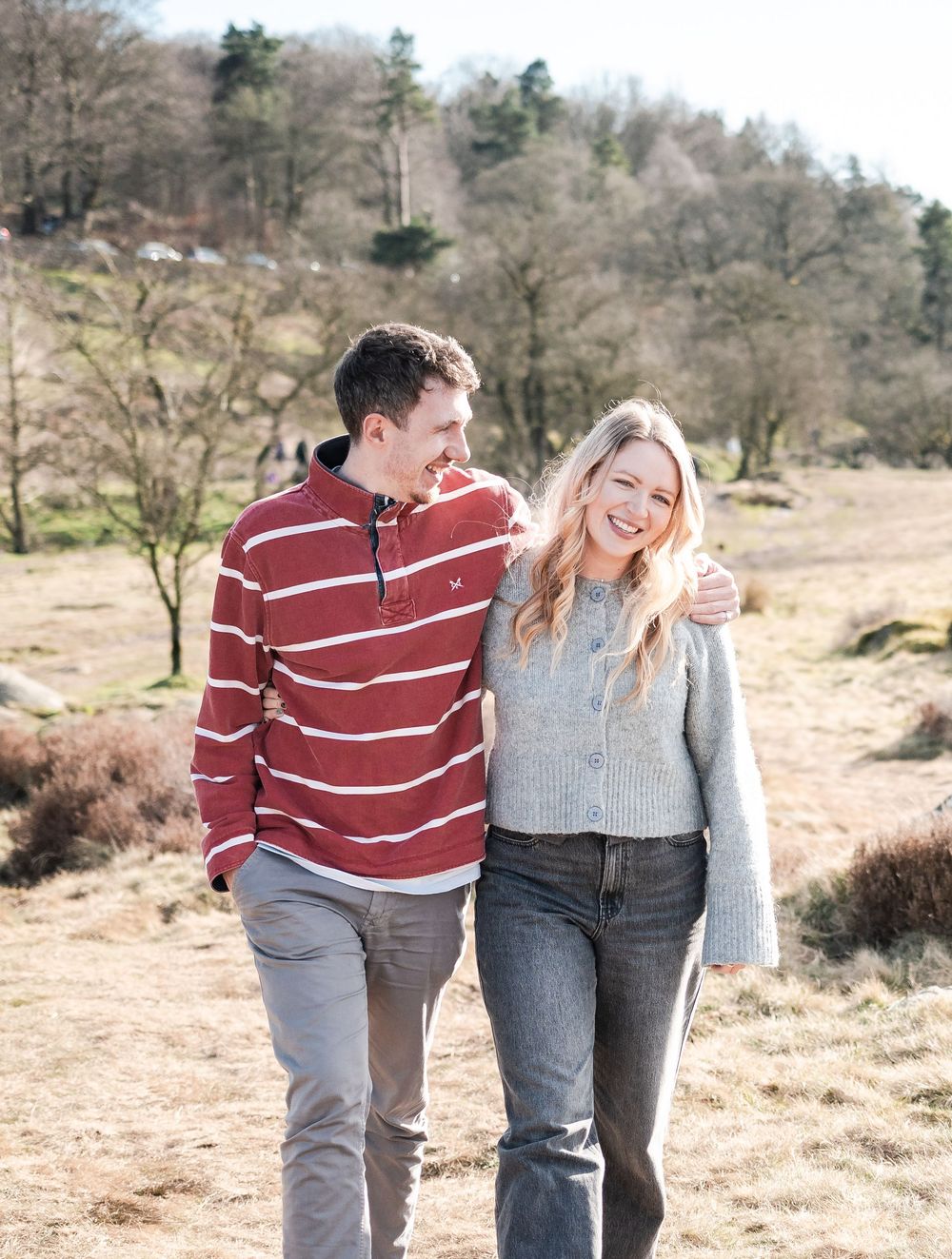 A couple walks together and shares a playful moment in a scenic winter landscape with bare trees and sandy ground.