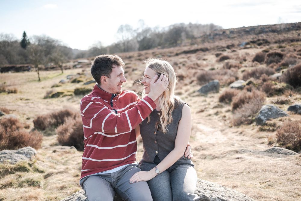 A couple sits on rocky terrain sharing a romantic moment during their engagement session at golden hour.