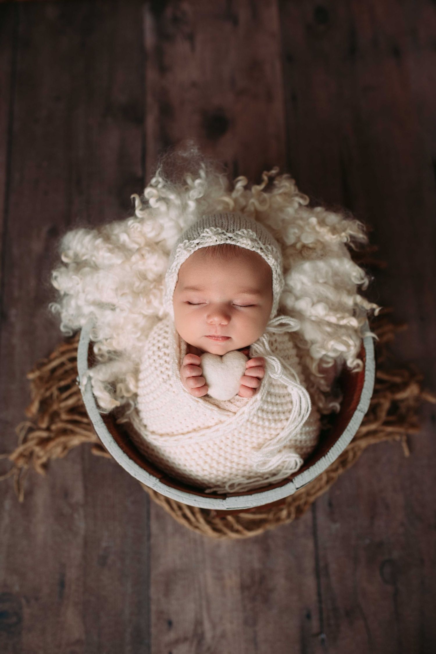 Sleeping newborn swaddled in a delicate, boutique wrap, posed in a cozy basket in studio newborn photography Woodbury MN