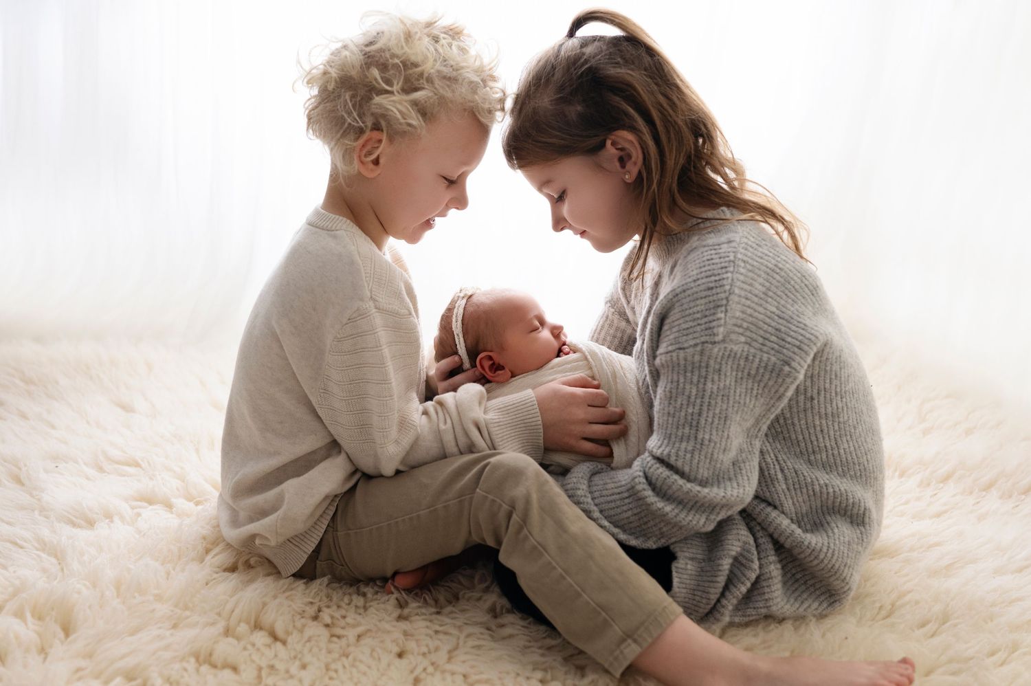 Siblings gently kissing a newborn’s forehead – heartwarming family newborn photography in Woodbury MN