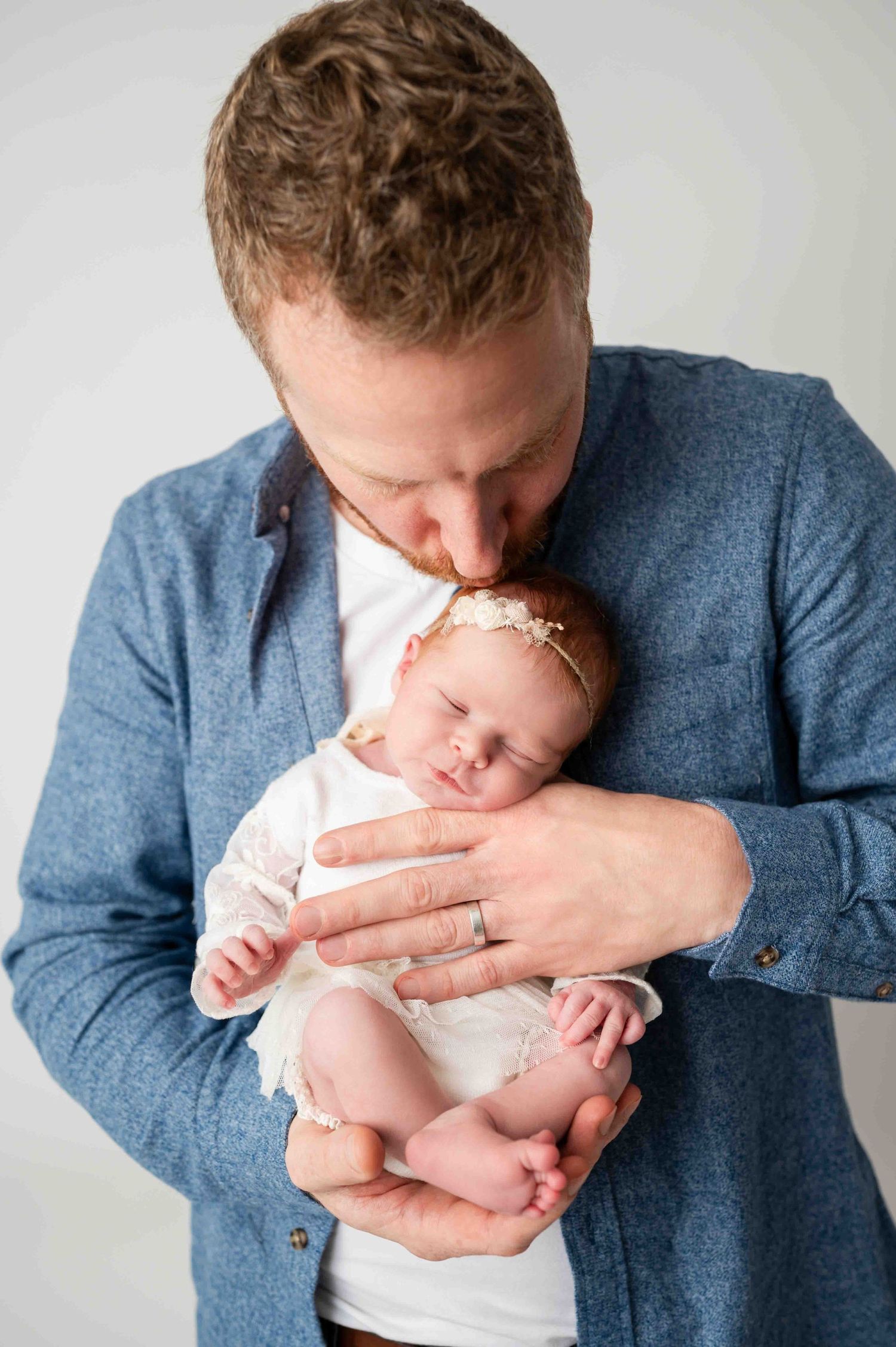 father holding and kissing his baby in his arm and smiling during the newborn session in Woodbury MN