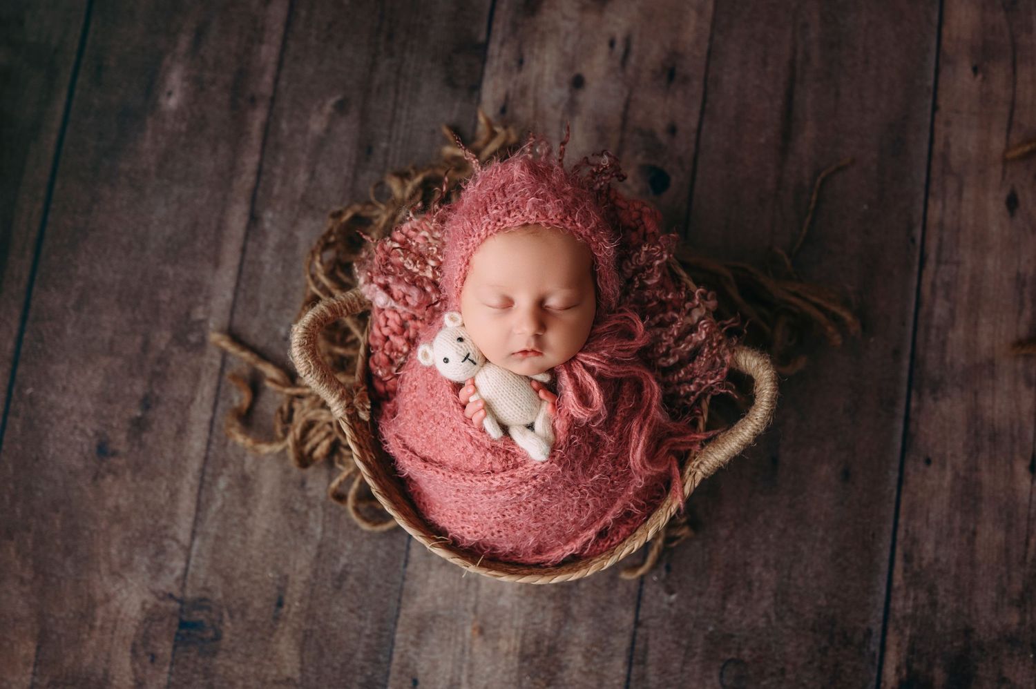 Sleeping newborn swaddled in a delicate, boutique wrap, posed in a cozy basket in studio newborn photography Woodbury MN